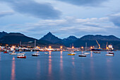 Hafenstadt in blauer Stunde mit anlegenden Booten und sich im Wasser spiegelnden Straßenlaternen, Ushuaia, Tierra del Fuego, Argentinien