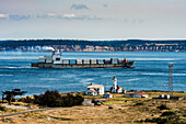 Freighter ship entering the Puget Sound via Admiralty Inlet from the Straight of Juan de Fuca. The Point Wilson Lighthouse is located on the Fort Worden Historical State Park near the town of Port Townsend. Whidbey Island is in the background,Washington,United States of America