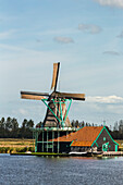 Historische hölzerne Windmühle entlang des Flusses Zaan mit blauem Himmel und Wolken,Zaandam,Niederlande