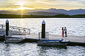 Frau und Mann stehen bei Sonnenuntergang auf einem Steg, Port Douglas, Queensland, Australien