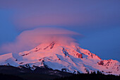 Der verschneite Mount Hood leuchtet bei Sonnenaufgang rosa mit einer Wolkenformation, die über dem Gipfel schwebt und ihn verdunkelt, Oregon, Vereinigte Staaten von Amerika