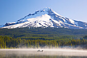 Majestätischer Mount Hood und Trillium Lake, mit aufsteigendem Nebel und Menschen, die in dem ruhigen Wasser Boot fahren und angeln, Oregon, Vereinigte Staaten von Amerika