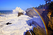 Regenbogen über den zerklüfteten Klippen an der Küste von Oregon, während sich die Wellen brechen und auf die Felsen plätschern,Oregon,Vereinigte Staaten von Amerika