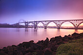 Yaquina Bay Bridge bei Sonnenuntergang mit warmem Licht, das sich auf dem ruhigen Wasser spiegelt, Newport, Oregon, Vereinigte Staaten von Amerika