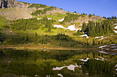 A tent set up on the water's edge of a tranquil Tipsoo Lake in the mountains with traces of snow on the slopes,Mount Rainier National Park,Washington,United States of America