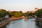 A passenger boat with tourists cruises along the Seine River while Parisians sit along the river banks.,Paris,France