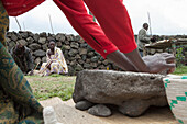 Zwischen zwei Felsen mahlt eine Frau Zutaten, die zum Kochen verwendet werden sollen,Volcanoes National Park, Ruanda