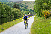 Eine Frau fährt mit dem Fahrrad auf dem Treidelpfad des Caledonian Canal in der Nähe von Fort Augustus, Schottland, Fort Augustus, Schottland