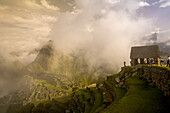 Touristen blicken vom Wachhaus über den nebelverhangenen Machu Picchu.