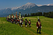 The procession to celebrate the Herz-Jesu Festival enters a large meadow overlooked by the Karwendel mountain range.,Austria.