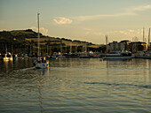 Sailing boat entering the port at sunset with green hills in the background,Porto San Giorgio,Marche,Italy