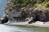 Two people sitting on a sandy beach at the base of rocky cliffs.,Cap-Bon-Ami,Forillon National Park,Gaspe Peninsula,Quebec,Canada.