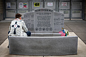 Junger Mann sitzt nachdenklich an einem Denkmal für amerikanische Kriegsveteranen, Bothell, Washington, Vereinigte Staaten von Amerika