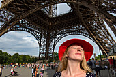 Junge Frau mit rotem Hut steht unter dem Eiffelturm und sonnt sich im Sonnenlicht in Paris,Frankreich,Paris,Frankreich