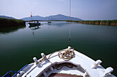 Blick auf ein flaches Meer, Boote und Hügel über den Bug eines weißen Segelboots, Republik Türkei