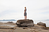 Frau steht auf einem Felsbrocken am Strand, Vancouver, BC, Kanada