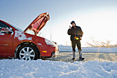 Mann telefoniert neben einem Auto mit offener Motorhaube im Winter