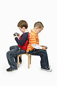 Jungen mit Handheld-Videospielen Rücken an Rücken sitzend