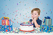 Kleiner Junge mit Geburtstagsgeschenken und einem Wunsch, bevor er die Kerzen auf der Geburtstagstorte ausbläst