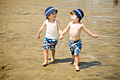 Zwillingsjungen gehen Hand in Hand am Strand spazieren