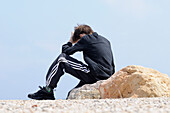 Boy Sitting on Rocks by Coast