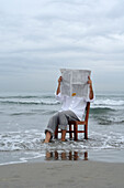 Mann sitzt auf einem Stuhl im Meer und liest eine Zeitung