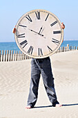 Junge hält eine große Uhr am Strand