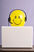 Smiley-Ballon mit Headset an Laptop-Computer