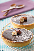 Close-up of Chocolate Tarts on Cooling Rack Topped with Nuts and Icing Sugar