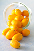 Close-up of Bowl of Kumquats Spilling on Blue Background,Studio Shot