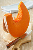 Close-up of Wedge of Pumpkin on Cutting board with Knife on Beige Background,Studio Shot