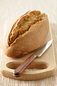 Close-up of Loaf of Bread with Knife on Cutting Board on Beige Background,Studio Shot