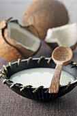 Kokosnussmilch in Schale mit Holzlöffel, Kokosnüsse im Hintergrund
