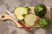 Draufsicht auf runde Zucchini auf Schneidebrett mit Messer, eine halbiert