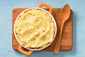 Overhead View of Dish of Mashed Potatoes on Cutting Board with Wooden Spoon