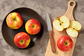 Draufsicht auf Äpfel auf Teller und Schneidebrett mit Messer, ein halbierter Apfel