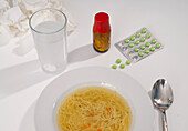 Medikamente, Schüssel mit Hühnersuppe und Glas Wasser auf dem Tisch, Studioaufnahme