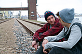 Zwei Teenager sitzen zusammen auf Eisenbahnschienen, in der Nähe des Hafens, Deutschland