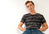 Portrait of young man sitting and leaning against wall,looking at camera,studio shot on whire background