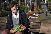 Teenager sitzt auf einer Bank auf dem Friedhof