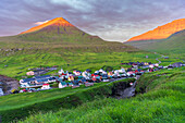 Die bunten Häuser des Dorfes Gjogv mit den von der frühen Sonne beleuchteten Bergen, Blick auf den Sonnenaufgang, Insel Eysturoy, Färöer Inseln, Dänemark, Europa