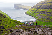 Ein Mann steht auf einem Felsen und bewundert das Dorf Tjornuvik bei nebligem Wetter, Sunda Kommune, Streymoy Insel, Färöer Inseln, Dänemark, Europa