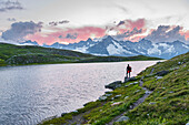 Hiker stands near the shore of Fenetre lake admiring the sunset over the massif of Mount Blanc,Ferret valley,Valais canton,Col du Grand-Saint-Bernard (St. Bernard mountain pass),Switzerland,Europe