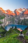 View of a hiker resting in front of the Oeschinensee lake surrounded by snowy peak at sunset,Oeschinensee,Kandersteg,Bern Canton,Switzerland,Europe