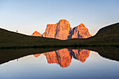 Wanderer bewundert den Sonnenuntergang vor dem riesigen Pelmo-Massiv, das sich im Wasser des kleinen Sees von Baste spiegelt, Giau-Pass, Cortina d'Ampezzo, Dolomiten von Belluno, Veneto, Italien, Europa