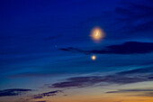 Die Konjunktion der zunehmenden Mondsichel mit Venus (hell und unten) und Mars (schwach und links) am 21. Juni 2023, dem Abend der Sommersonnenwende, mit den Welten in den Wolken am bunten Dämmerungshimmel. Auf der dunklen Seite des Mondes ist trotz der verdeckenden Wolken gerade noch der Erdschein zu erkennen.
