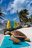 Palmen und eine Meeresschildkrötenstatue vor einem 3-D-Schild am Strand von San Pedro auf Ambergris Caye, Belize.