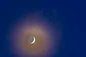 The conjunction of the waxing 4-day-old crescent Moon below the Pleiades,and set in a slightly hazy sky on March 25,2023. The haze adds the colourful "lunar corona" halo around the bright crescent of the Moon from diffraction effects in the high icy clouds. Shot before the sky got dark,the remaining twilight adds the blue to the background sky. Earthshine is visible on the dark side of the Moon.