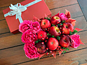 Gift box with arrangement of apples, roses and rose hips