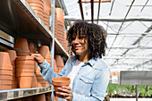 Smiling young woman in nursery at shelf with clay pots